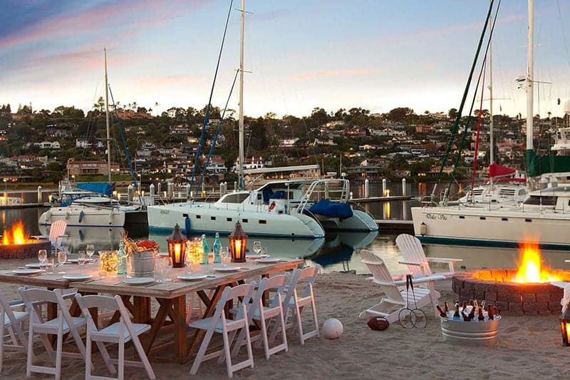 Dining and seating area with a firepit next to boats stationed on the water