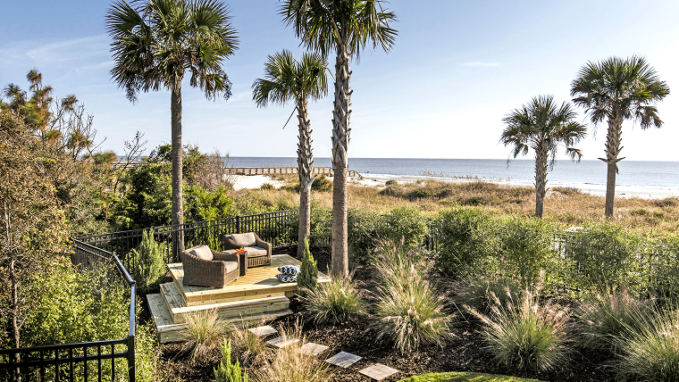 seating area among palm trees and greenery next to the beach at a Noble House Hotels & Resorts property